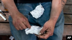 Seorang pria menyiapkan bahan-bahan untuk menghisap fentanil di sebuah taman di Portland, Oregon, pada 18 Mei 2023. (Foto: Beth Nakamura/The Oregonian via AP)