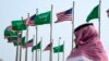 Seorang pria berdiri di bawah bendera AS dan Arab Saudi sebelum kunjungan Presiden Joe Biden, di sebuah lapangan di Jeddah, Arab Saudi, 14 Juli 2022. (Foto: AP)