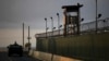 FILE - A U.S. soldier stands in the turret of a vehicle with a machine gun, left, as a guard looks out from a tower at the Guantanamo Bay prison in Cuba, March 30, 2010.