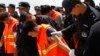 Chinese, in an orange vest, arrested over an alleged internet scam, are escorted by Chinese police officers before boarding at Phnom Penh International Airport, in Phnom Penh, Cambodia, Thursday, Oct. 12, 2017. Cambodia has deported dozens of Chinese cit