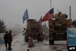 FILE - A line of US military vehicles drive through a checkpoint of the Internal Security Forces in Manbij as they head to their base on the outskirts of the northern Syrian city on Dec. 30, 2018.