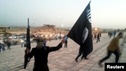 FILE - An Islamic State fighter holds an IS flag and a weapon on a street in the city of Mosul, June 23, 2014.