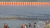 Sejumlah migran berjalan di antara kawat berduri dan pelampung di sepanjang perbatasan antara AS-Meksiko di sungai Rio Grande di Eagle Pass, Texas, pada 16 Juli 2023. (Foto: AFP/Suzanne Cordeiro)